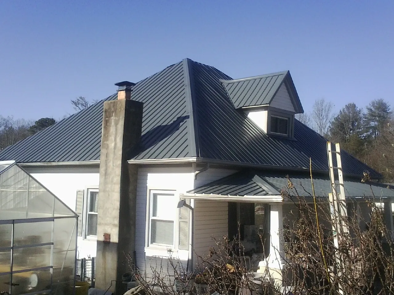 Dark blue standing seam metal roof on a white farmhouse with dormer — Slate & Tile Roof Repair by Roofing Brothers in Fairport