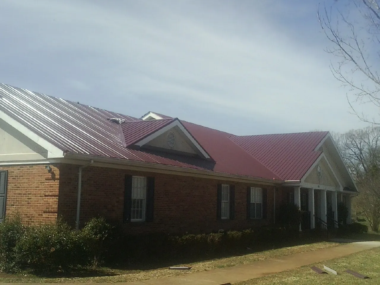 Red metal roof with gabled entries on a long brick building, from a Hail Damage Roof Repair job in Fairport