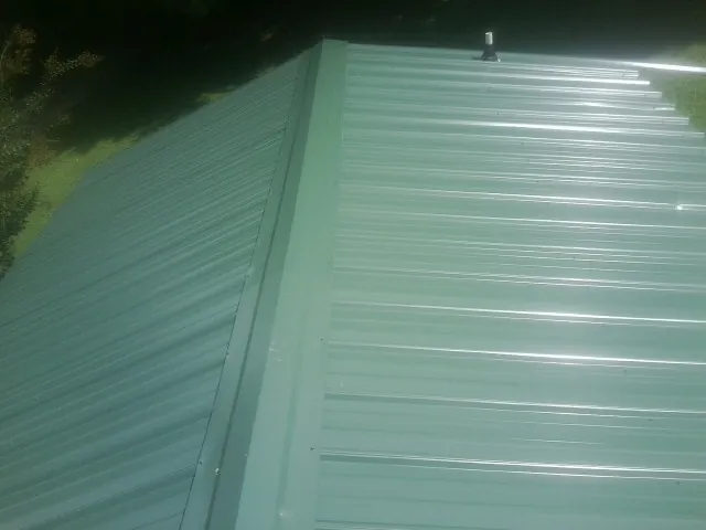New green metal panels meeting at the ridge of a roof — Flat Roof Repair work by our crew in Fairport