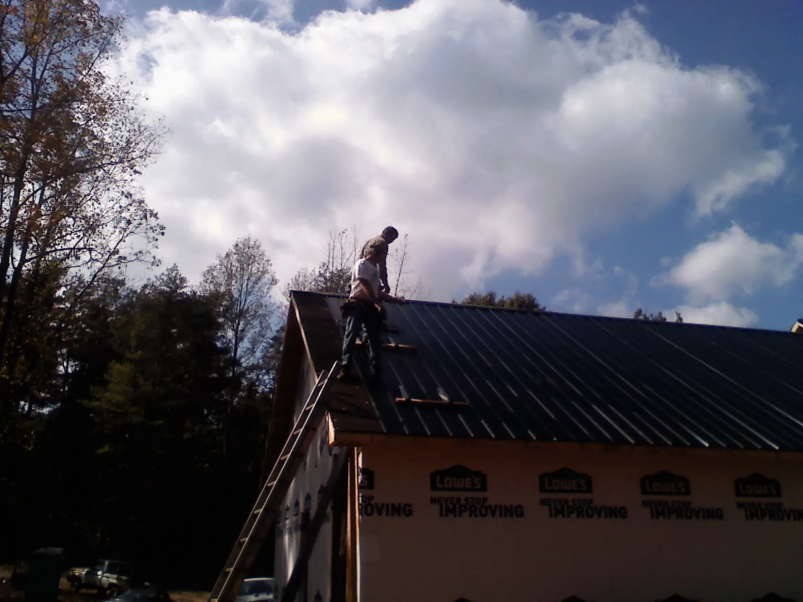 Roofer fastening dark metal panels high against a cloudy sky, from a Roof Inspection job in Fairport
