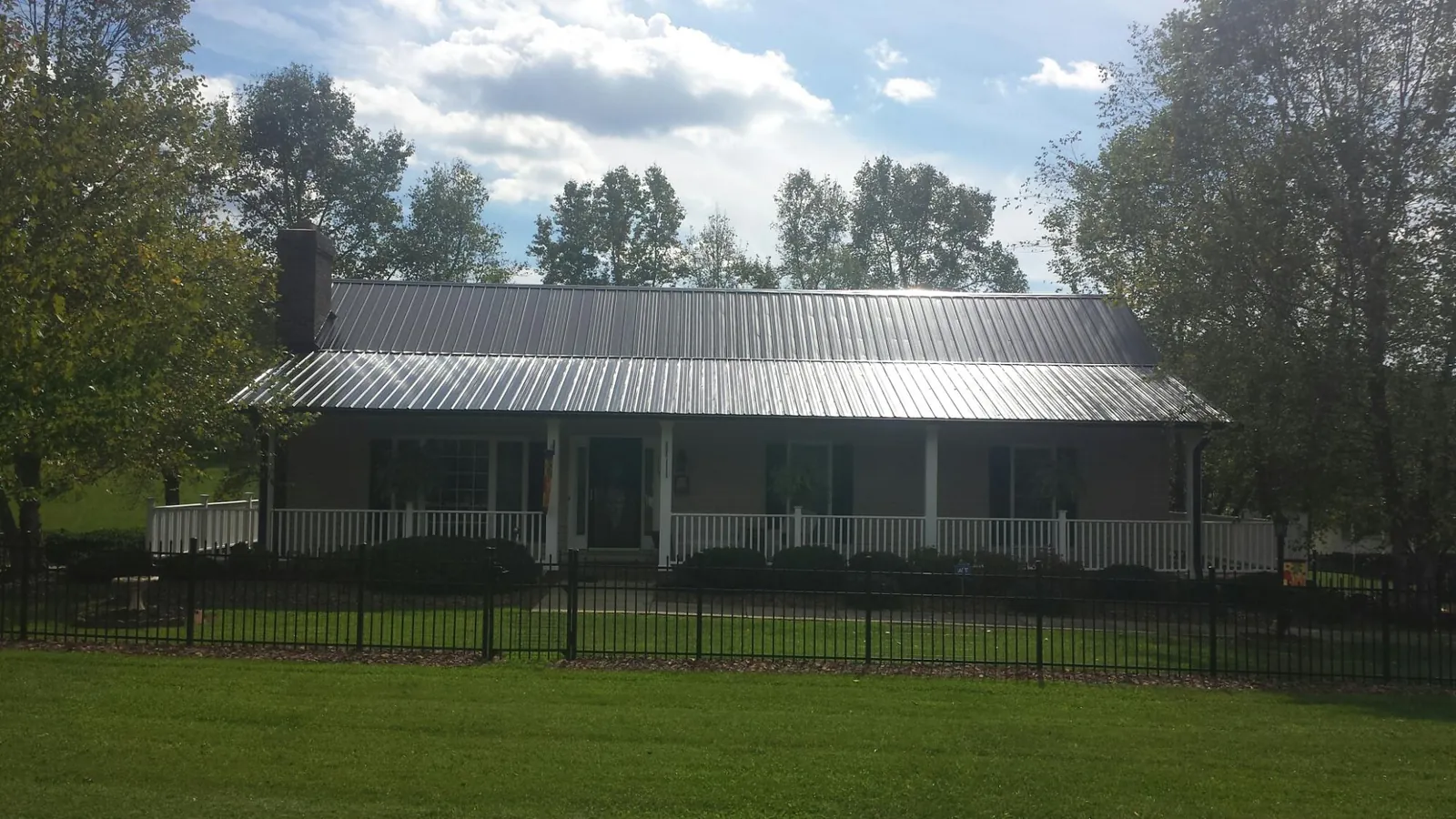 Gray metal roof on a brick ranch with a full width front porch — Gutter Guard Installation work by our crew in Fairport