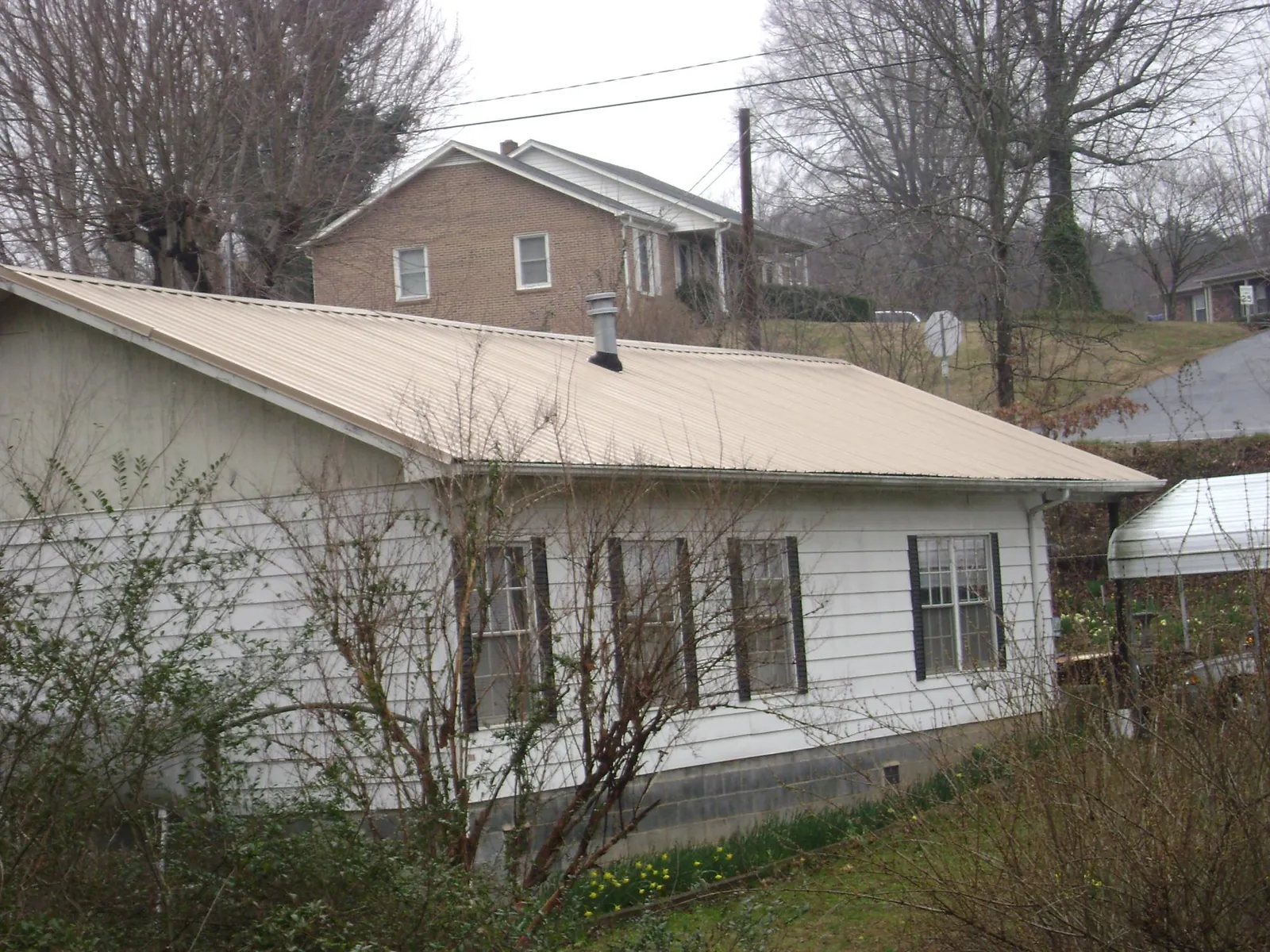Tan metal roof on a white sided house set into a hillside — Commercial Roofing by Roofing Brothers in Fairport