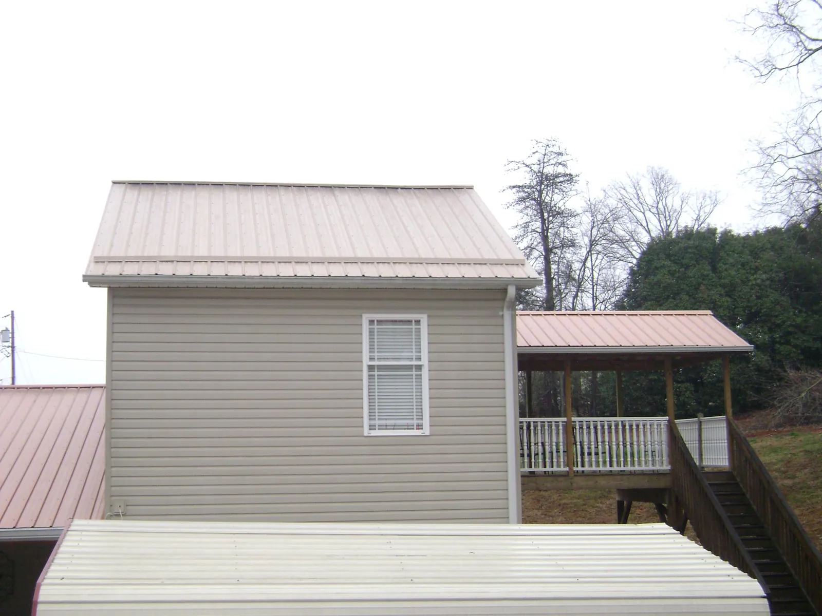 Tan metal roofs on a two story addition and attached porch, from a Roof Replacement job in Fairport
